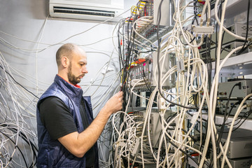 Worker works on the control panel in the data center. Specialist connects coaxial television wires in the rack of the TV station server room. Man switches  audio and video cable on the patch panel.