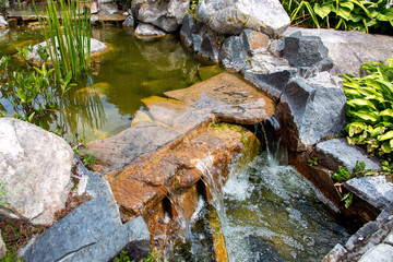 waterfall on stone artificial pond with flow water in the park on a day, closeup.