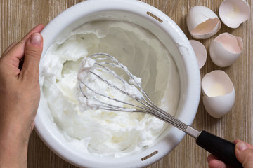 Hand of woman holding beater with whisked egg whites in the bowl