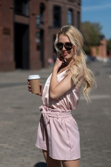 beautiful blonde girl walks around city with glass take-away coffee. Resting, sunny day