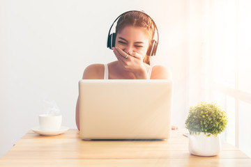 Asian girl wearing a white singlet. She put her hand over her mouth and laughed happily as she watched online movies on the streaming media system in the bedroom while drinking coffee in the morning.