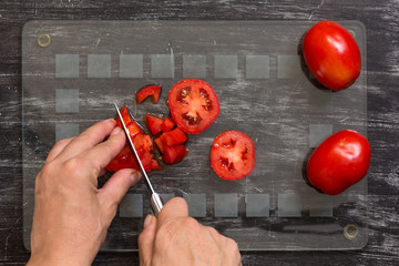 Hand of woman cutting fresh tomatoes with knife on the glass cut board on black background