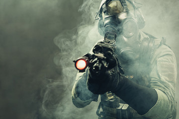 Special force soldier with gasmask between smoke at battlefield is aiming the target