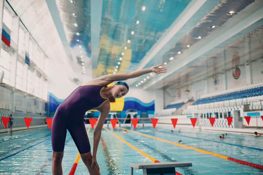 Young woman swimmer warming up before swim in swimming pool