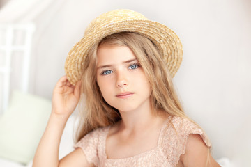 Close up Portrait face of cute girl in straw hat. Thoughtful little blonde with long hair sits on bed in bright children's room. Childhood concept. child dreams.  Provence style. relaxation, rest