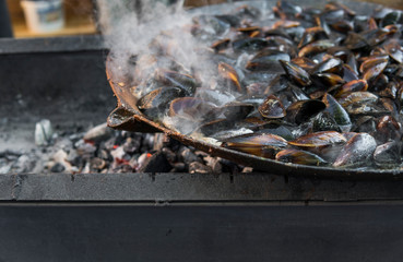 Fresh mussels at grill pan. Seafood barbecue outdoors. Picnic healthy food, mussels in shells. Plenty of mussel shells cooking at large metallic pan.