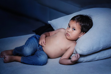 Three year old boy laying in  a couch holding his tummy, having nighttime stomach pains with an upset facial expression.