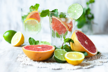 Refreshing healthy alcohol free home made citrus lemonade with pepper mint, limes, lemons, pomelo. Lace napkin, white wooden background. Vacation mood, enjoying summertime, health caring lifestyle