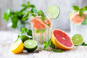 Refreshing healthy alcohol free home made citrus lemonade with pepper mint, limes, lemons, pomelo. Lace napkin, white wooden background. Vacation mood, enjoying summertime, health caring lifestyle