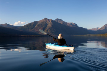 Adventurous Man Kayaking in Lake McDonald during a sunny summer evening with American Rocky Mountains in the background. Taken in Glacier National Park, Montana, USA.