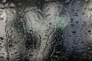 Drops of rain flow down the glass of a car