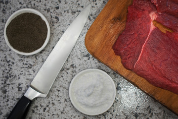 knife, salt, pepper and meat on kitchen board viewed from zenith angle