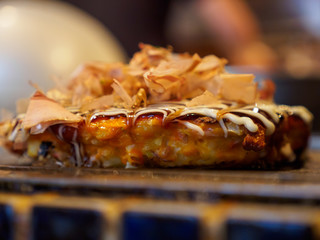Macro detail of a freshly cooked Okonomiyaki with Katsuobushi, dried fish flakes, sauce, and mayonnaise, on a Teppan grill. Shallow focus. Dotonbori, Osaka, Japan. Travel and cuisine.