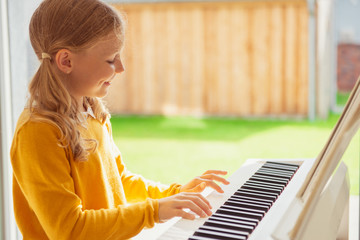 Portrait of pretty little girl having piano lesson at modern white e-piano