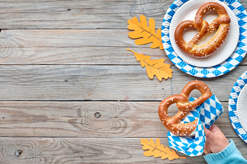 Oktoberfest, pretzels on disposable plates, hand holding a pretzel and Autumn leaves with copy-space
