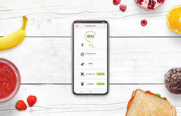 Phone on desk surrounded with food. Healthy life app concept with daily number of steps, number of calories burned, number of calories consumed and the amount of water.