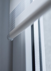 Details of white fabric roller blinds on the white plastic window in the living room. Close up on...