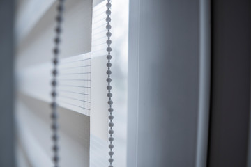 Details of white fabric roller blinds on the white plastic window in the living room. Close up on roll curtains indoor.