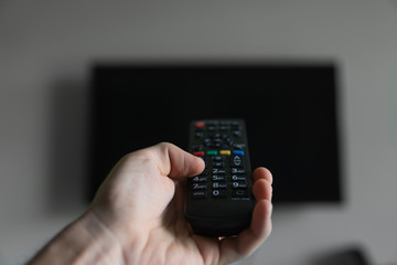 The man with the remote control in hand want switch on the TV and presses the button on the remote control. Remote control in hand closeup.