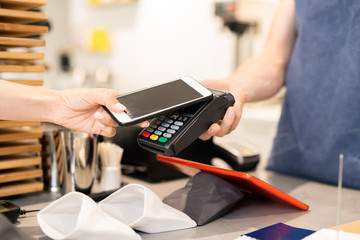 Hand of young woman holding smartphone close to electronic payment machine