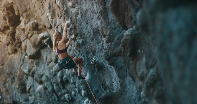 Cinematic slow motion rock climbing - fit attractive woman sport climbing with golden light