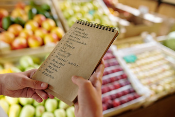 Notepad with list of products to buy in supermarket held by youthful girl