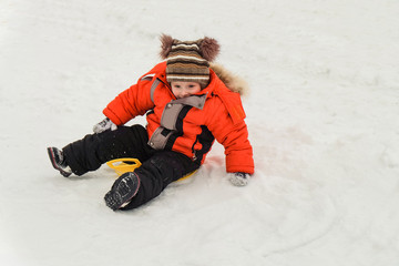 Fototapeta na wymiar Little boy rides on an ice-boat from a snow slide. Sledding snow saucer - winter childrens fun. Winter activity.