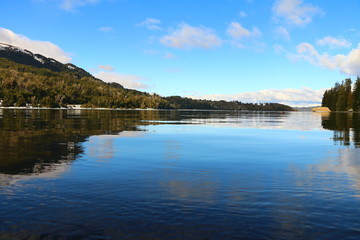 lago de aguas cristalinas y reflejo perfecto, rodeado de bosques de pinos y barcos flotando, en Bahia Manzano cerca de  Villa La Angostura, Patagonia Argentina