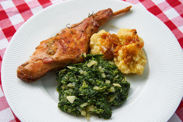 Close up Picture of roasted rabbit leg, marinated in garlic and rosemary served with spinach, chopped onion and potato dumplings on white plate. Simple and healthy traditional dish of Czech cuisine.