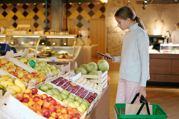 Casual youthful girl taking photo of fresh ripe fruits on display
