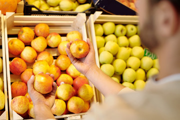 Young man choosing fresh ripe yellow apples while standing by fruit display