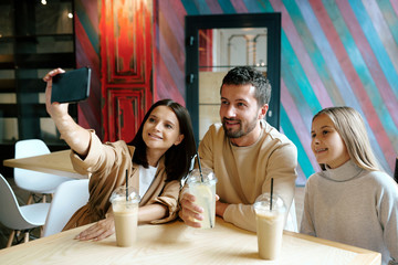 Young cheerful family of three resting by table in cafe after shopping
