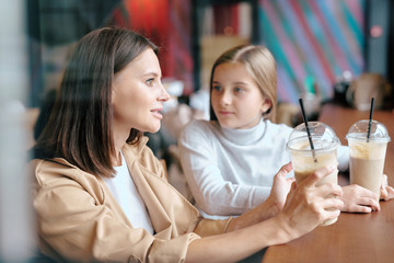 Pretty young woman with milk cocktail talking to her daughter in cafe