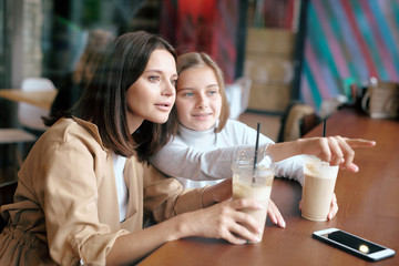 Youthful girl showing her mom something curious behind window in cafe