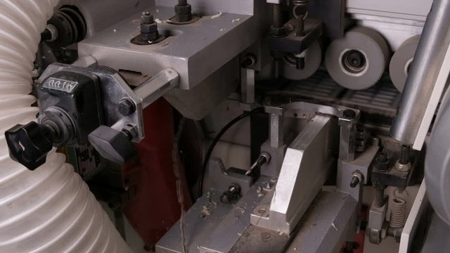 Close-up of the reverse side of the edge banding machine. Automatic gluing, trimming brown pvc edges and chamfering in furniture production. A detail of white chipboard rolls on casters.