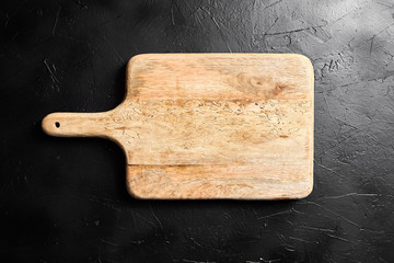 A Cutting board with handle on black stone table. Empty pine wooden chopping board on dark background, top view