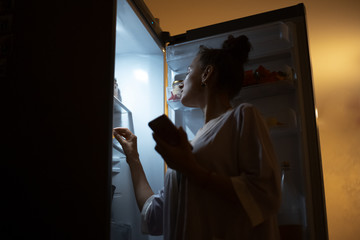 Young girl looking in fridge at night.
