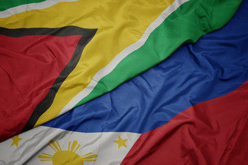 waving colorful flag of philippines and national flag of guyana.