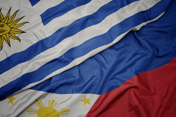 waving colorful flag of philippines and national flag of uruguay.