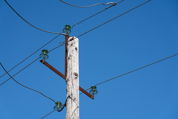 Old wooden power pole with wires on insulators against clear cloudless blue sky