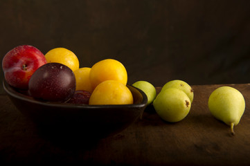 Various autumn fruits, red and yellow plums, and green pears in a bowl