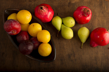 Various autumn fruits, red and yellow plums, green pears and pomegranates in a bowl