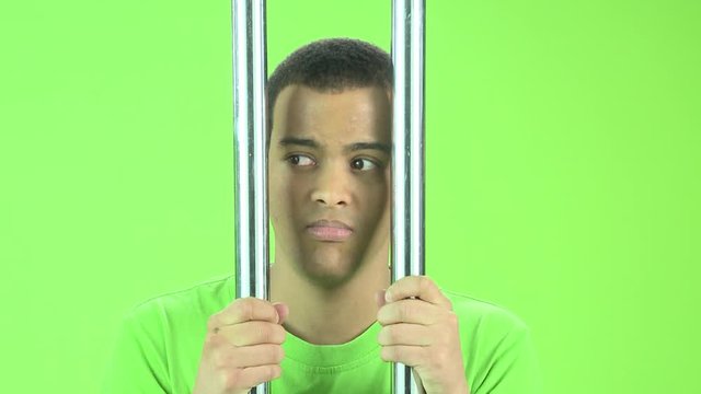 Man On Chroma Green Screen In Green T-shirt In Prison Setting Behind Bars