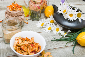 treatment and prevention of seasonal colds, natural products, health care, dried fruits and various useful herbs for health, a teapot with daisies, tea, on a wooden table, jars and a bowl