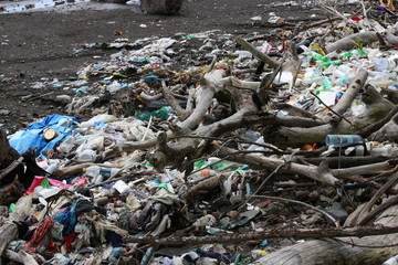Obraz premium Huge messy pile of plastic and trash litter among wood branch debris polluting bare brown sand beach environment near ocean