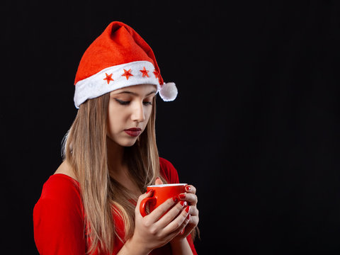 Beautiful girl posing with hot drink in red mug on the black background in New Year outfit.
