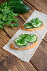 Delicious sandwiches for a snack on the board. Slices of white bread with sprat paste, cucumber and parsley. Cold appetizer on a vintage wooden table. 