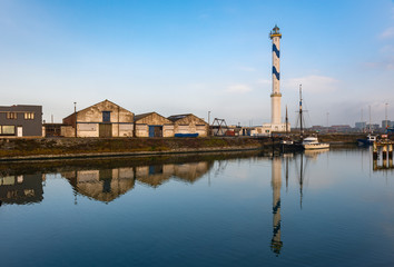 Naklejka premium The famous lighthouse of Ostend (Oostende) city with a reflection in one of the commercial docks of the harbor, West Flanders, Belgium.