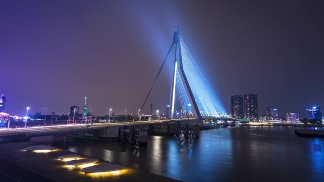 Amazing view of Maas river in night Rotterdam, Netherlands. Romantic atmosphere in city center. Colorful illumination of Erasmus Bridge (Erasmusbrug) reflecting in water and lighting sky. Time lapse