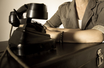 Woman with a vintage suitcase and a phone is waiting for a phone call.